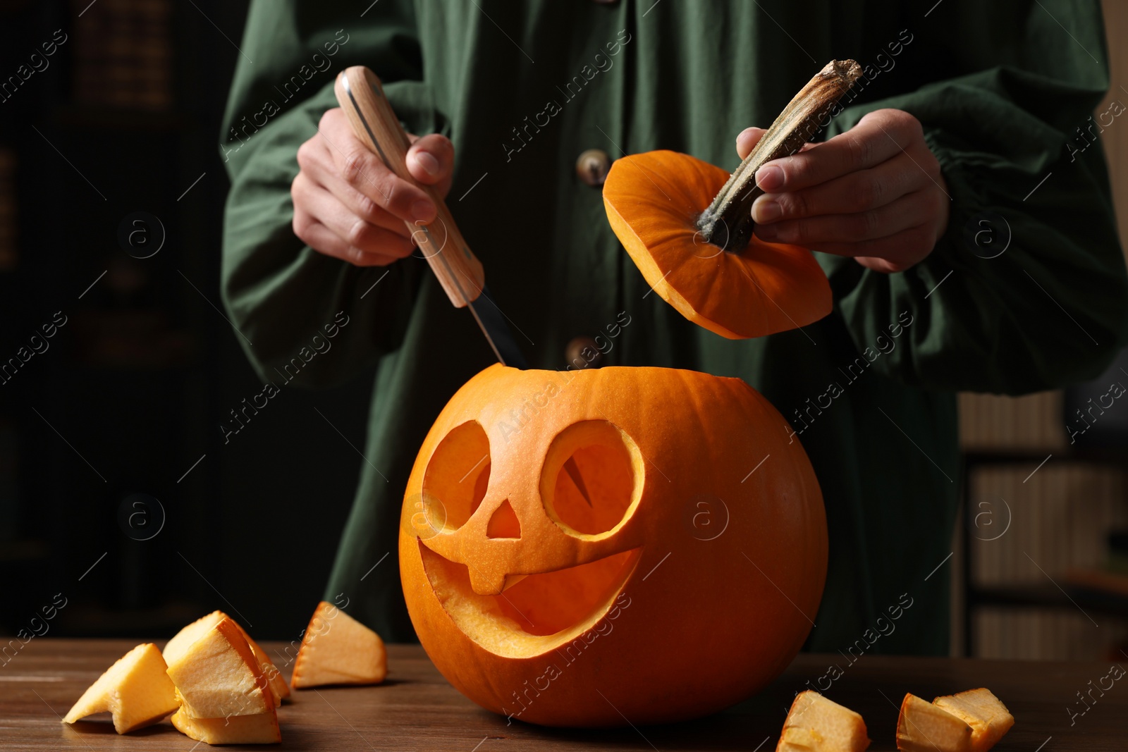 Photo of Woman carving pumpkin for Halloween at wooden table, closeup