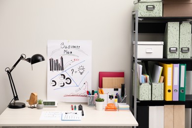 Photo of Business process planning and optimization. Workplace with plan, lamp, notebook and stationery on white wooden table