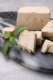 Photo of Pieces of tasty halva and mint served on light grey table, closeup