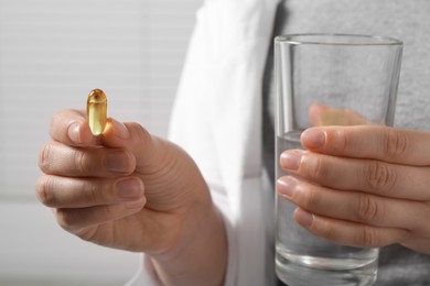 Photo of Woman with glass of water and pill on light background, closeup