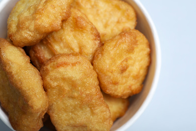 Photo of Bucket with delicious chicken nuggets on light background, closeup