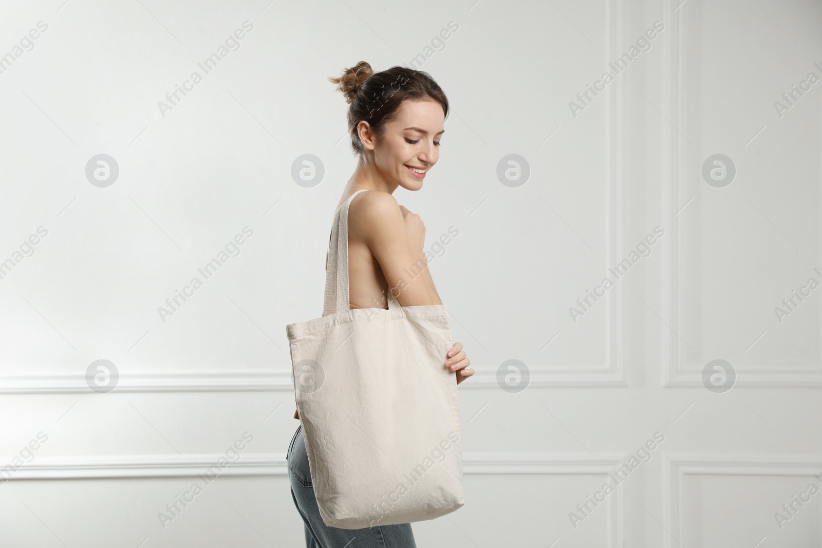 Photo of Happy young woman with blank eco friendly bag near white wall