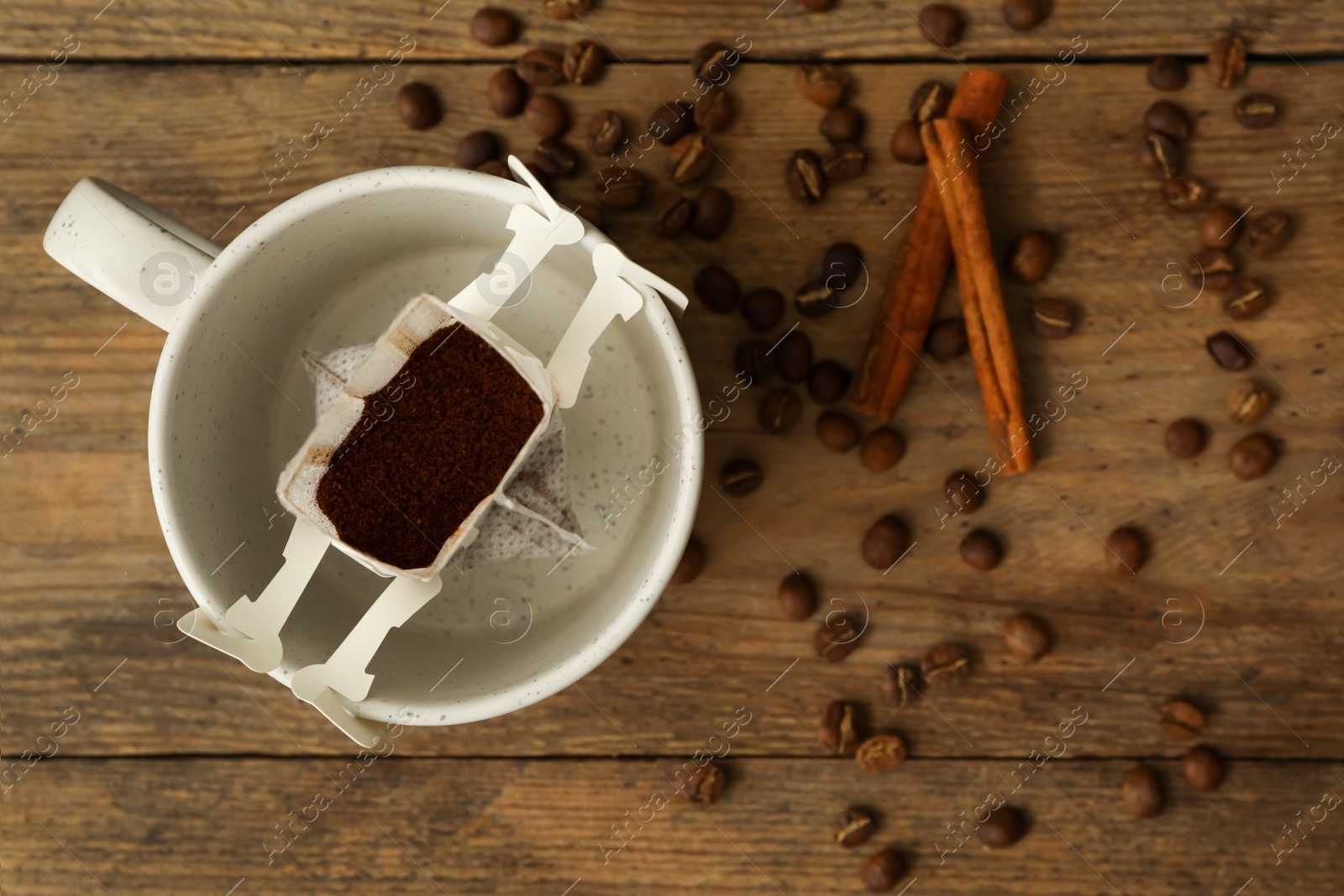 Photo of Drip coffee in cup, beans and cinnamon on wooden table, flat lay