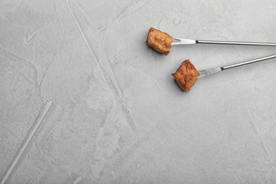 Forks with fried meat fondue pieces on grey background, top view. Space for text