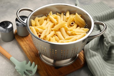 Delicious penne pasta in colander, spices and spoon on gray table