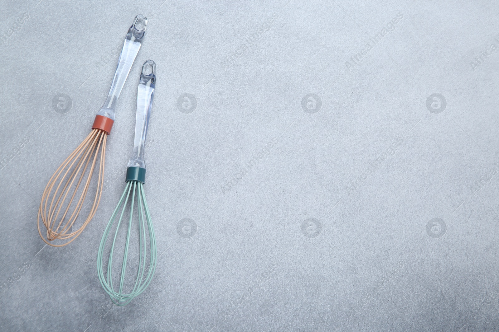 Photo of Two whisks on gray table, top view. Space for text