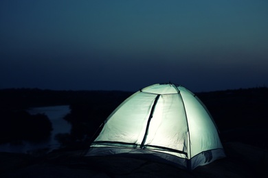 Photo of Small camping tent glowing in twilight outdoors. Space for text