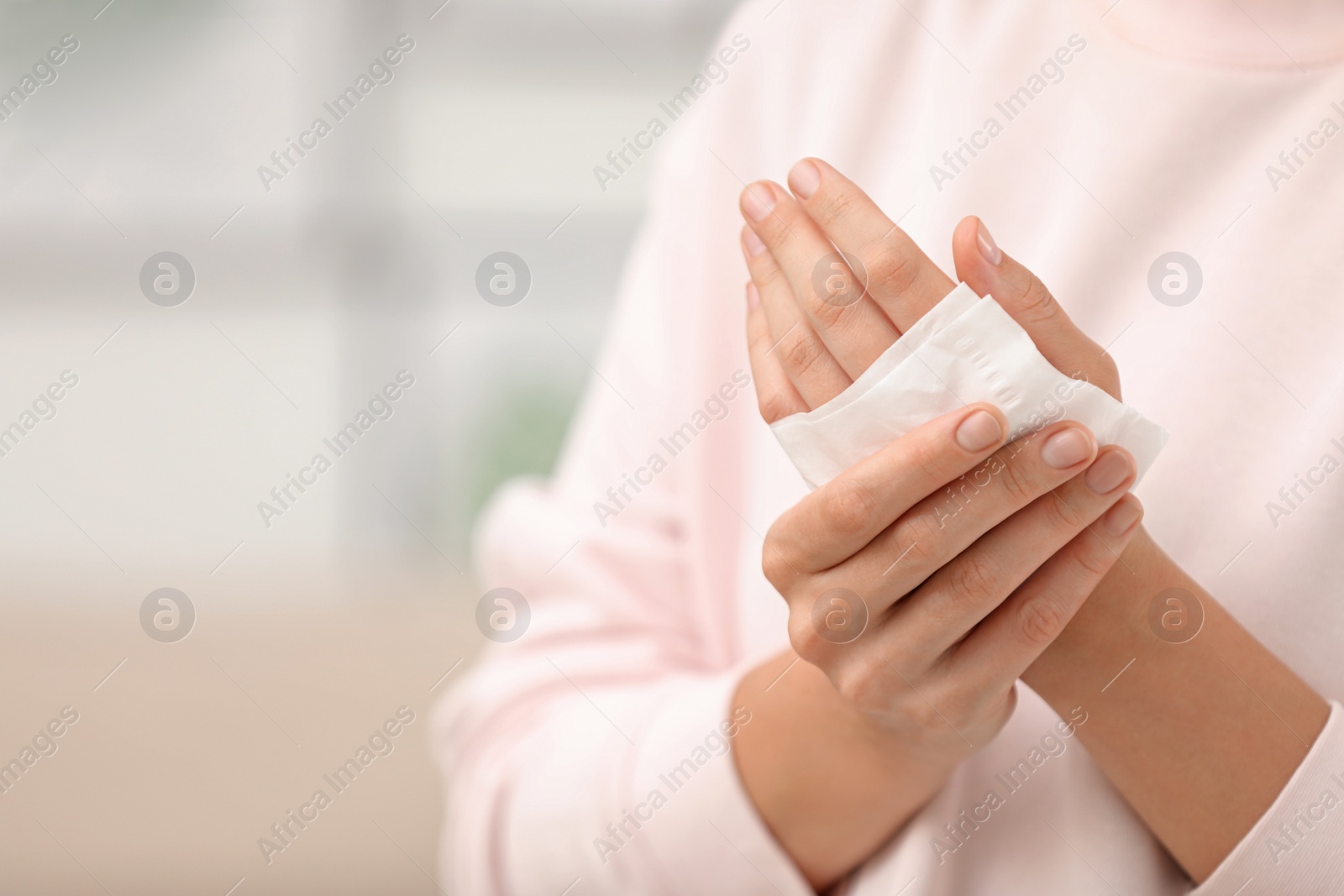 Photo of Woman cleaning hands with paper tissue on blurred background, closeup