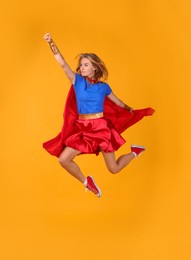 Photo of Confident woman in superhero costume jumping on yellow background
