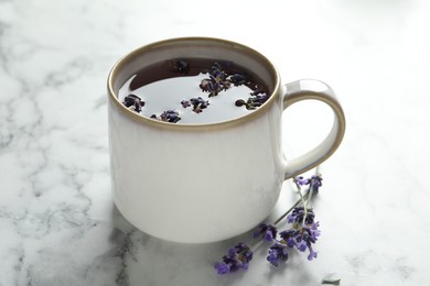 Photo of Fresh delicious tea with lavender and beautiful flowers on white marble table