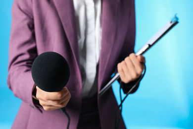 Professional journalist with clipboard and microphone on light blue background, closeup