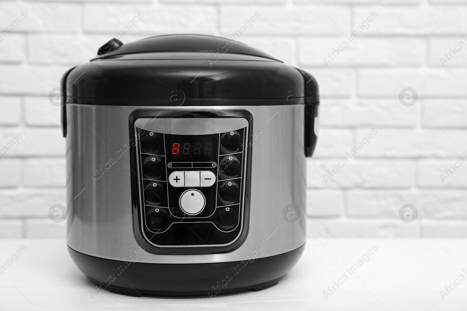 Photo of Modern electric multi cooker on table near brick wall
