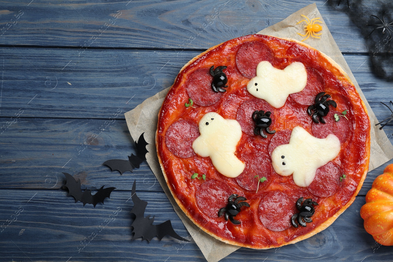 Photo of Cute Halloween pizza with ghosts and spiders served on blue wooden table, flat lay