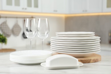 Photo of Clean plates, glasses and butter dish on white marble table in kitchen