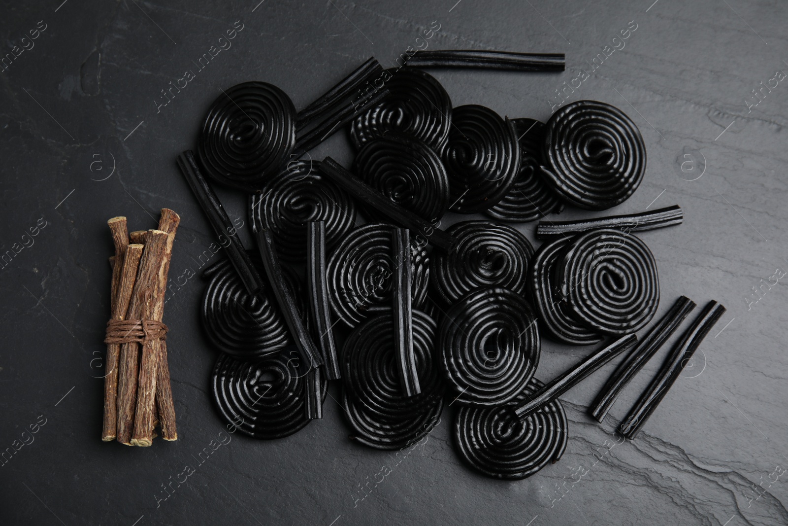 Photo of Tasty candies and dried sticks of liquorice root on black table, flat lay