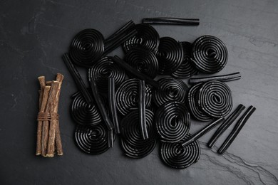 Photo of Tasty candies and dried sticks of liquorice root on black table, flat lay