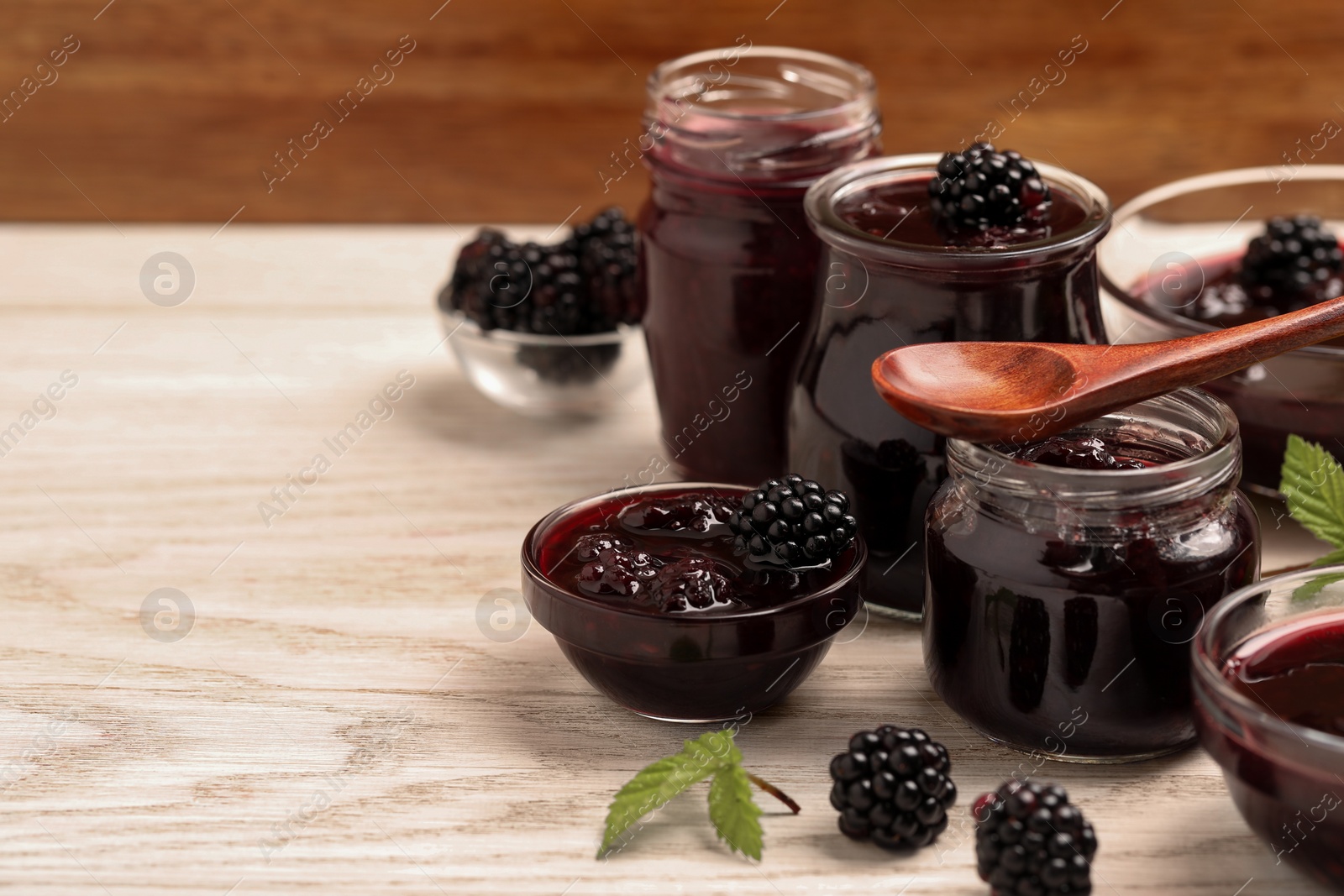 Photo of Tasty blackberry jam and fresh berries on white wooden table. Space for text