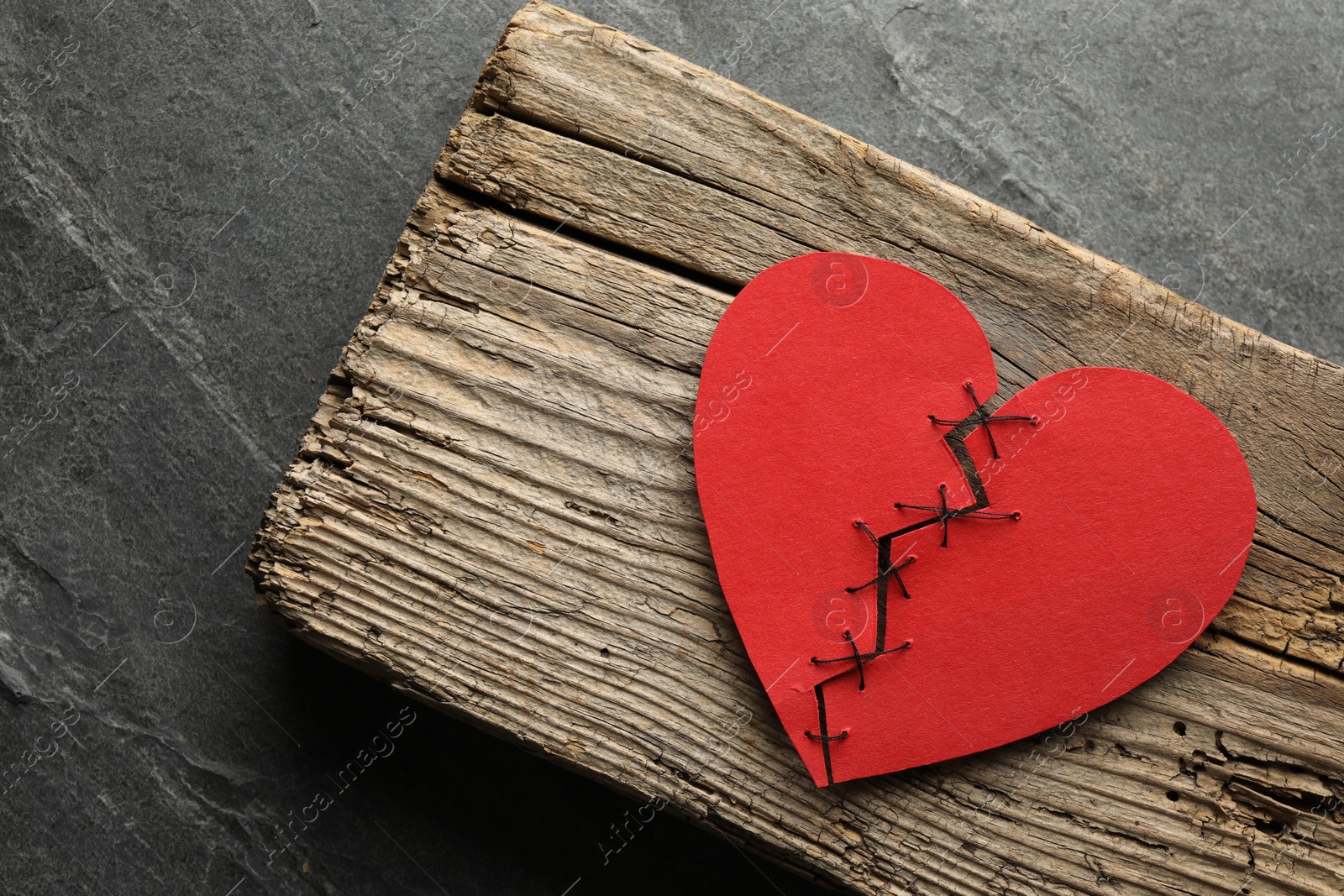 Photo of Broken heart. Torn red paper heart sewed with thread on grey table, top view