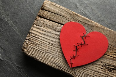 Photo of Broken heart. Torn red paper heart sewed with thread on grey table, top view