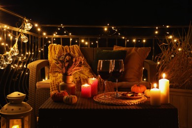 Glasses of wine, burning candles and autumn decor on outdoor terrace in evening