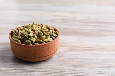 Photo of Dry cardamom pods in bowl on wooden table. Space for text