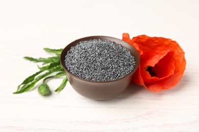 Photo of Bowl of poppy seeds and flower on white wooden table