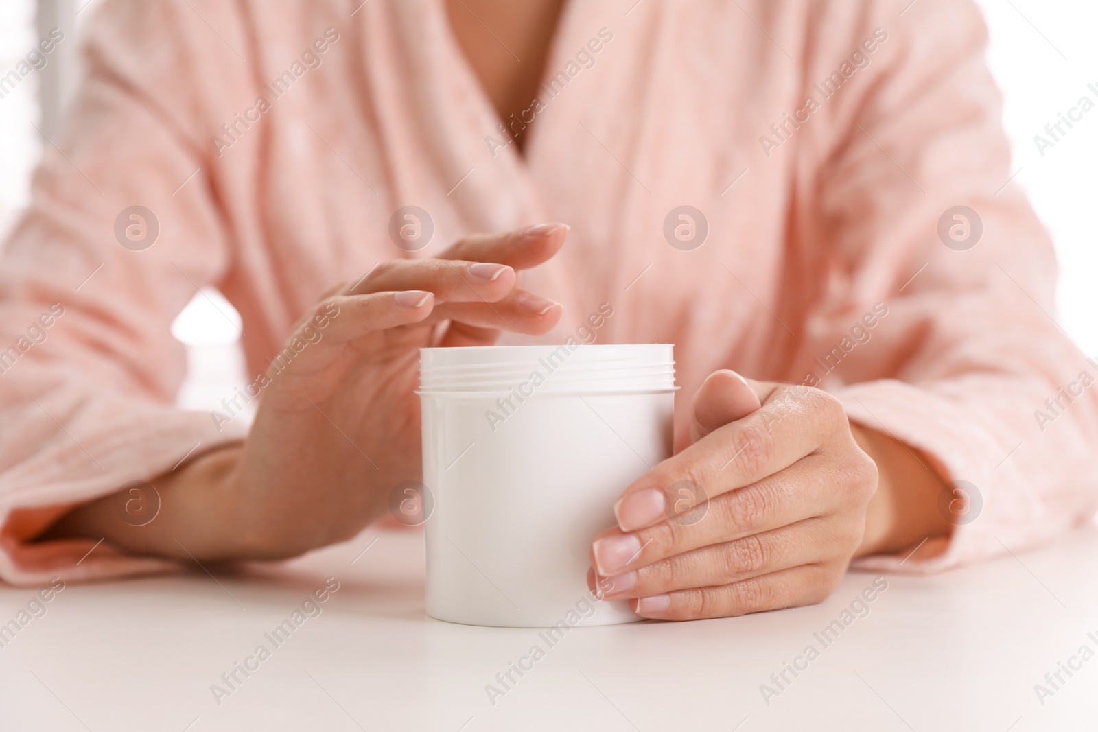 Photo of Woman with jar of moisturizing cream at white table, closeup