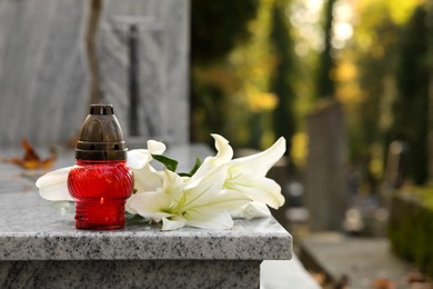 Photo of White lilies and grave lantern on granite tombstone outdoors, space for text. Funeral ceremony