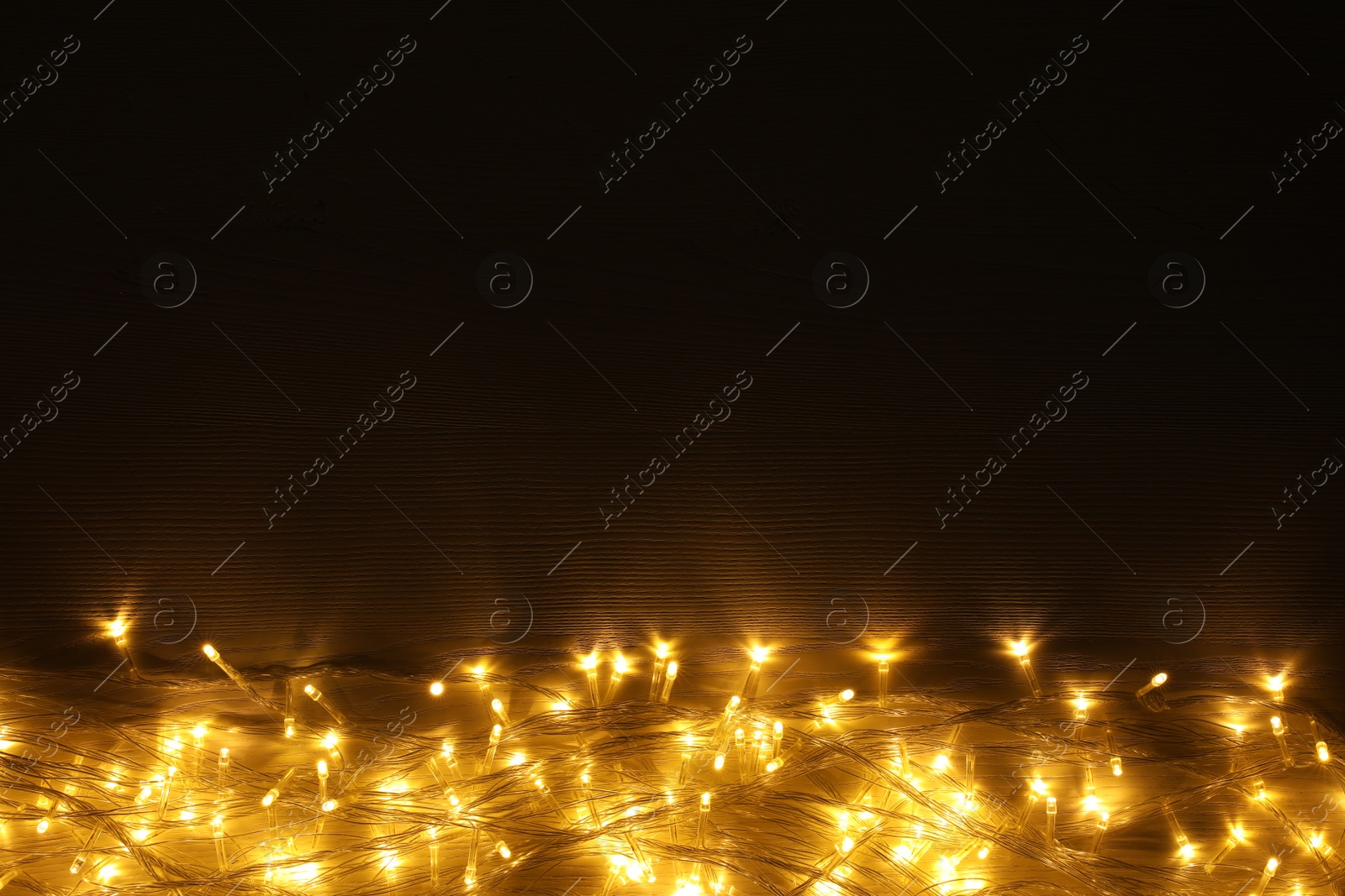 Photo of Beautiful glowing Christmas lights on wooden table, top view. Space for text