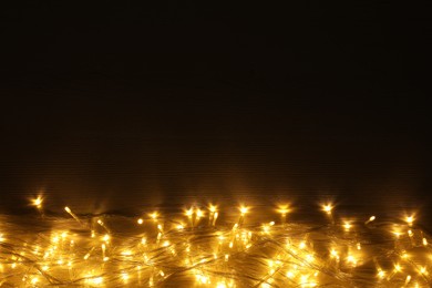 Photo of Beautiful glowing Christmas lights on wooden table, top view. Space for text