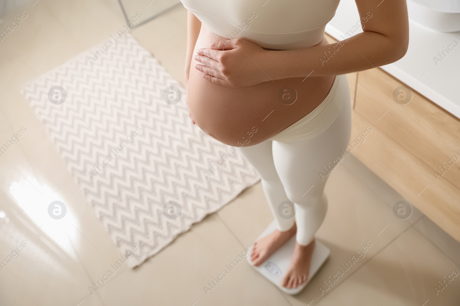 Photo of Pregnant woman standing on scales at home, closeup