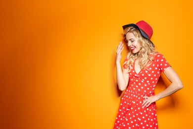 Stylish young woman with hat posing on color background