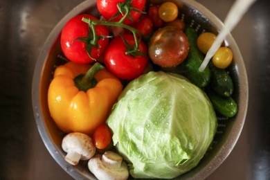 Washing different vegetables with tap water in metal colander inside sink, top view