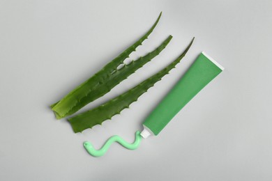 Tube of toothpaste and fresh aloe on light grey background, flat lay