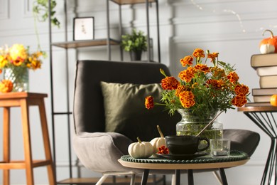 Photo of Beautiful autumn flowers, cup of drink and pumpkins on coffee table indoors, space for text