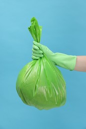 Photo of Woman holding plastic bag full of garbage on light blue background, closeup