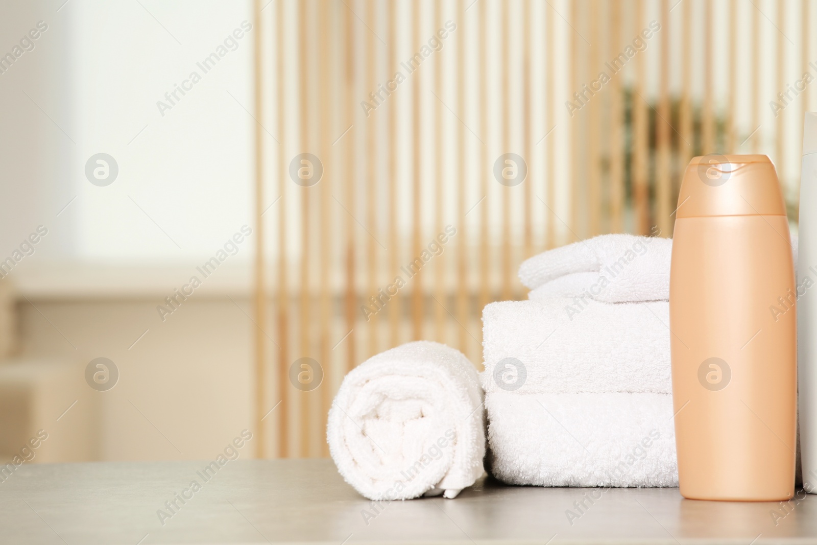 Photo of Soft folded terry towels and cosmetic bottle on light gray table indoors, space for text