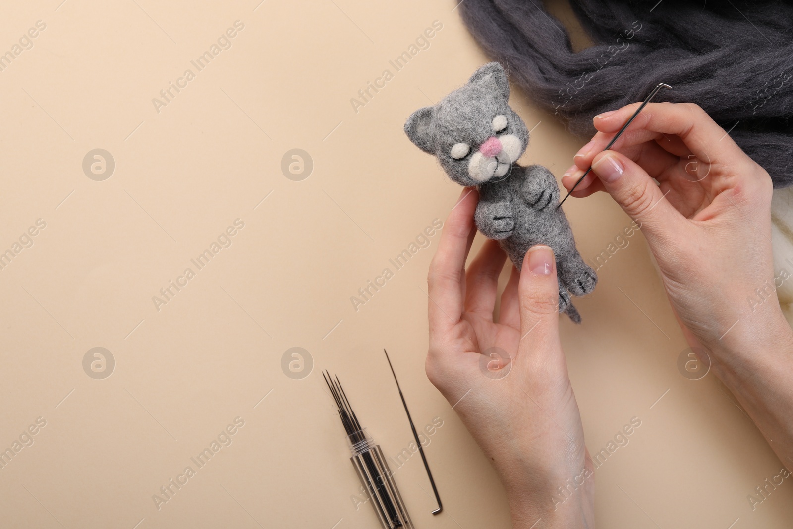 Photo of Woman felting toy cat from wool at beige table, top view. Space for text