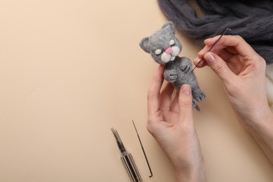 Photo of Woman felting toy cat from wool at beige table, top view. Space for text