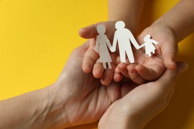 Mother and child holding paper cutout of family on yellow background, closeup