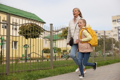 Being late for school. Senior woman and her granddaughter with backpack running outdoors, low angle view