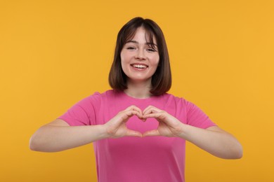 Photo of Happy woman showing heart gesture with hands on orange background