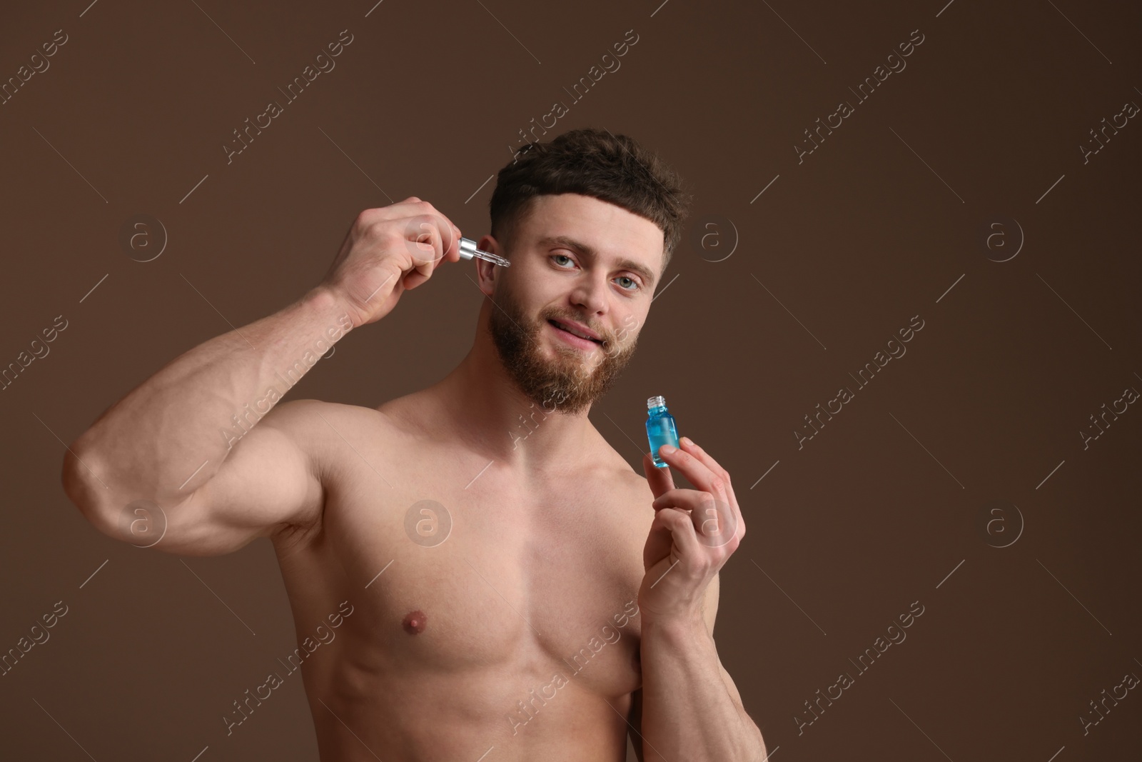 Photo of Handsome man applying serum onto his face on brown background, space for text