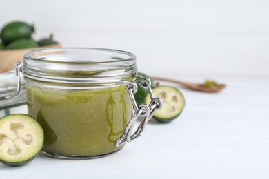 Photo of Feijoa jam in glass jar on white table, closeup. Space for text
