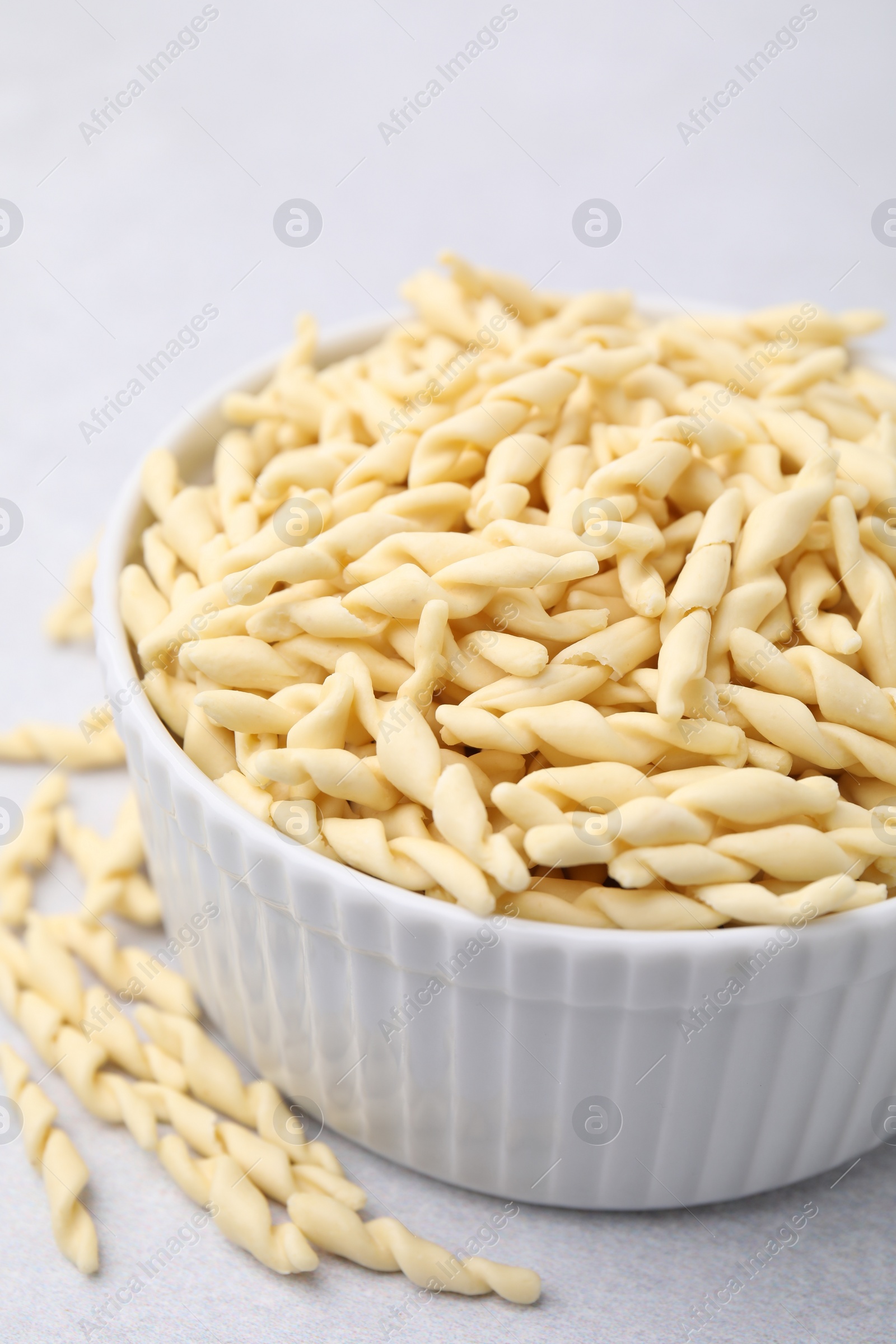 Photo of Bowl with uncooked trofie pasta on light grey table, closeup
