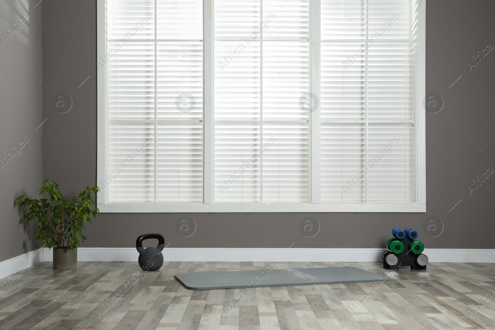 Photo of Exercise mat with different dumbbells and kettlebell in spacious room