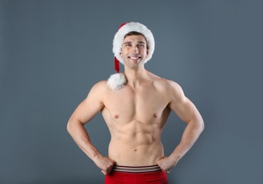 Photo of Young muscular man in Santa hat on gray background