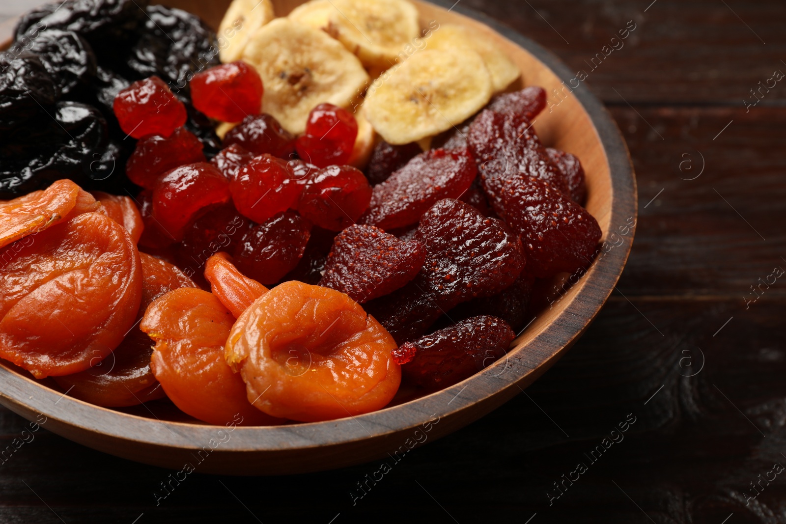 Photo of Mix of delicious dried fruits in bowl on wooden table, closeup