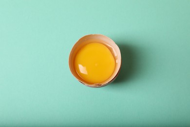 Photo of Cracked raw chicken egg with yolk on turquoise background, top view