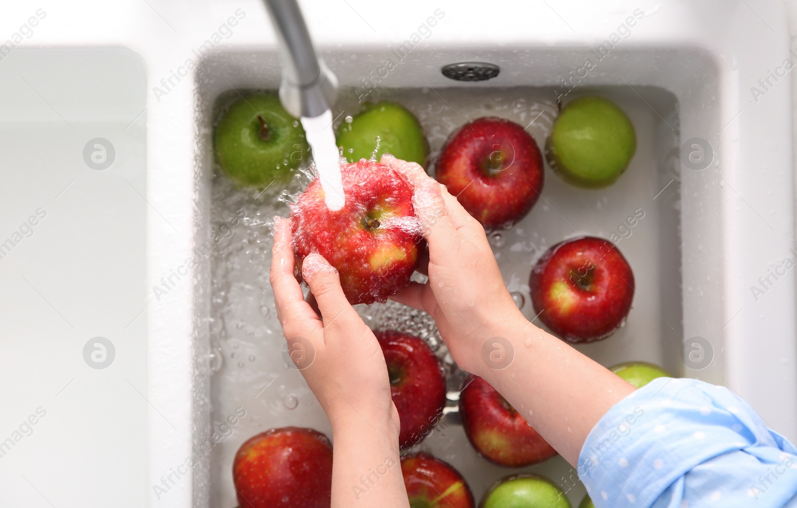 Photo of Woman washing fresh apples in kitchen sink, top view